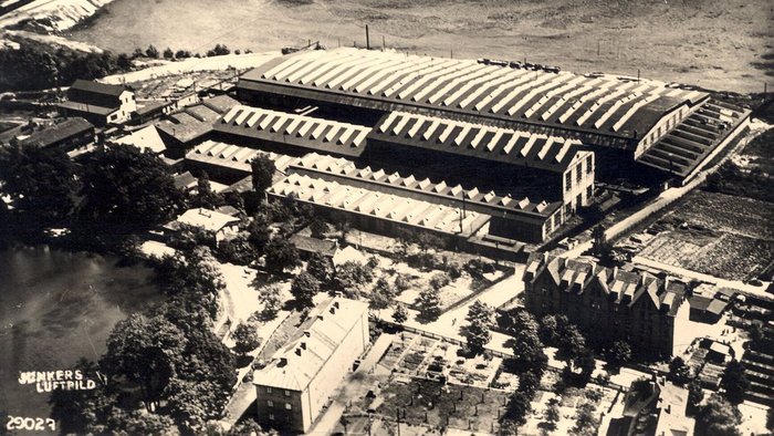 An aerial photograph from the 1930s showing the old factory, the former open-cast mine in the background and a pond.