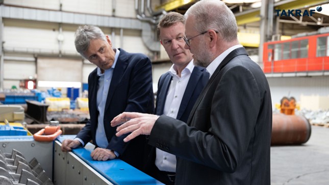 The picture shows TAKRAF Group CFO Massimo Valsecchi, CEO Thomas Jabs and Director Product Line TAKRAF Products and Aftermarket Matthias Gnilke standing in the production hall at a TAKRAF Sizer.